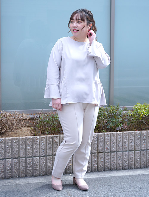 淡いグレージュのペプラムトップスを着て、同系色のセンタープレスパンツを履く女性