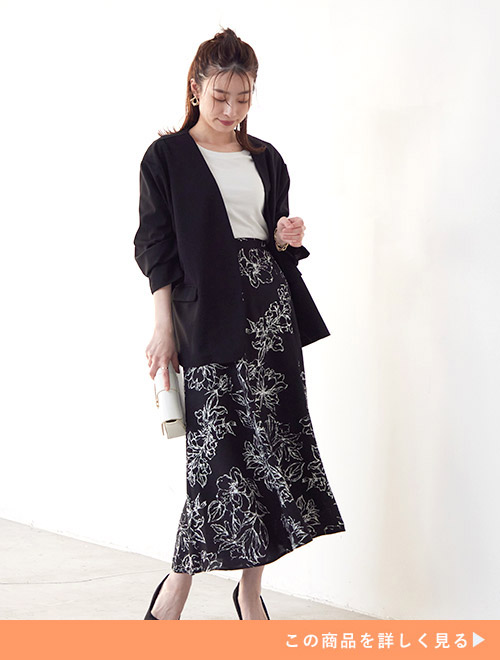 白のインナーに黒のジャケットを羽織り、花柄のスカートを履く女性