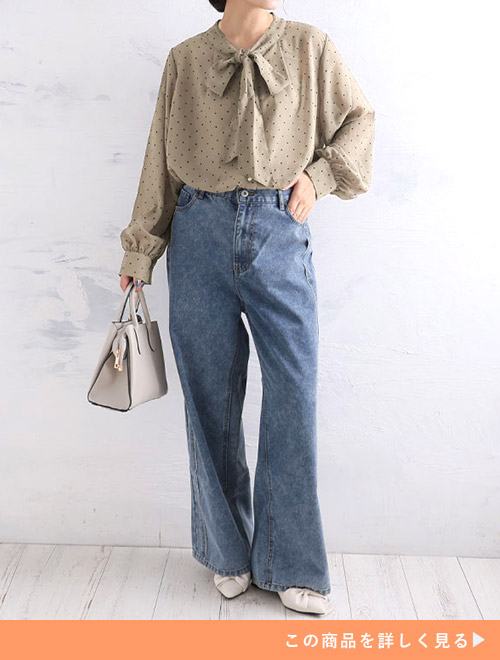 グレージュのドットブラウスとデニムパンツのコーデにホワイトバッグとパンプスを合わせる女性