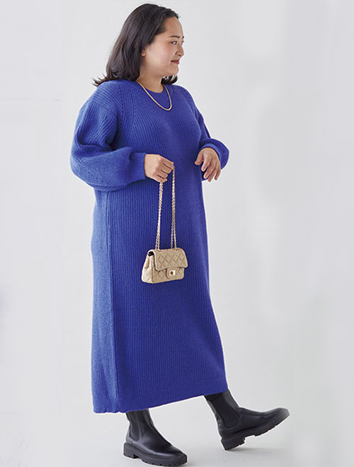 鮮やかなブルーのニットワンピースを着て、黒のサイドゴアブーツを履く女性