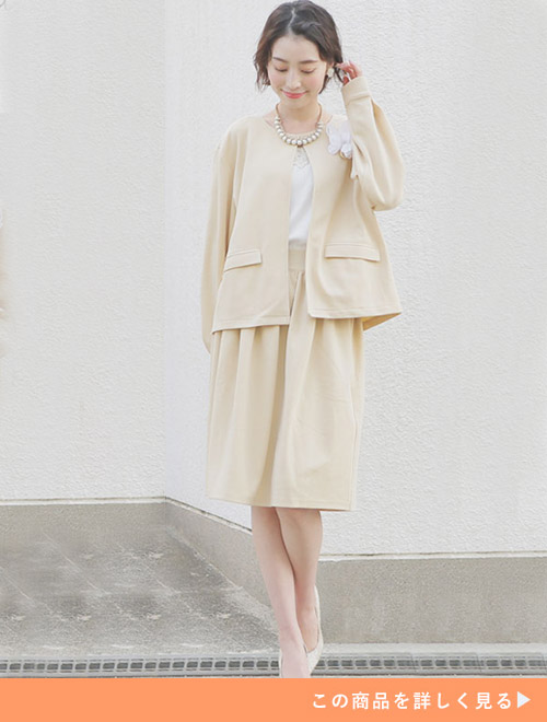 ベージュカラーのジャケット×膝丈スカートスーツに白色のトップスを合わせて着る女性