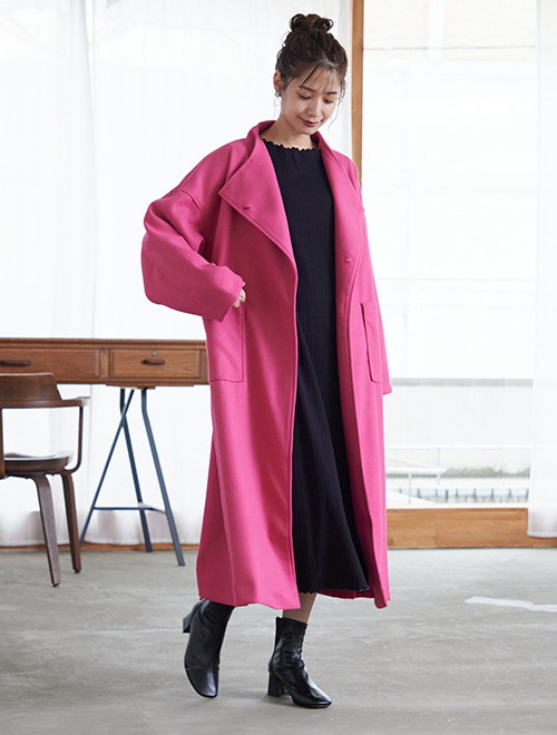 黒のワンピースに、ピンク色が鮮やかなビッグサイズのロングコートを羽織る女性