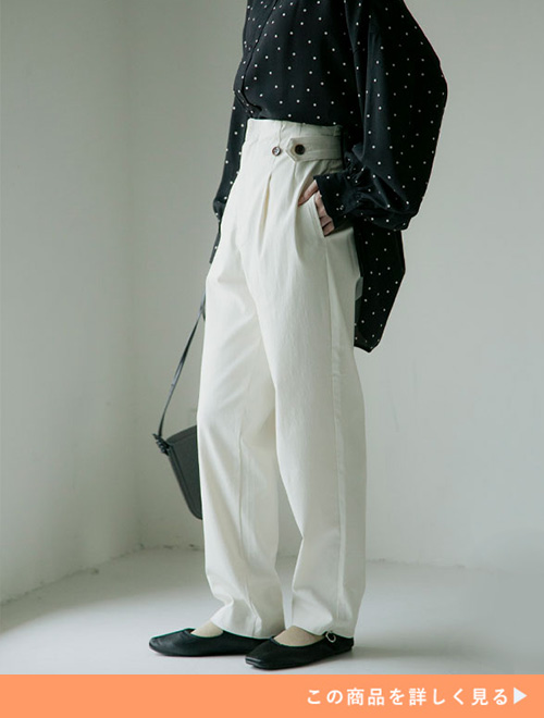 アイボリーのハイウエストパンツとブラックドットブラウスのコーデに、ブラックパンプスを履く女性