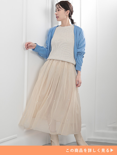 オフホワイトのチュールスカートとアイボリートップスのコーデにライトブルーのカーデを羽織る女性