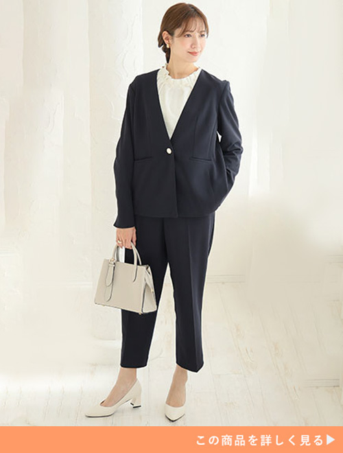 ネイビーのセットアップのインナーに、白のパール付きブラウスを着る女性