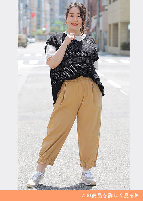 白T×ベージュのコクーンパンツに黒のレース編みベストを重ね着する女性