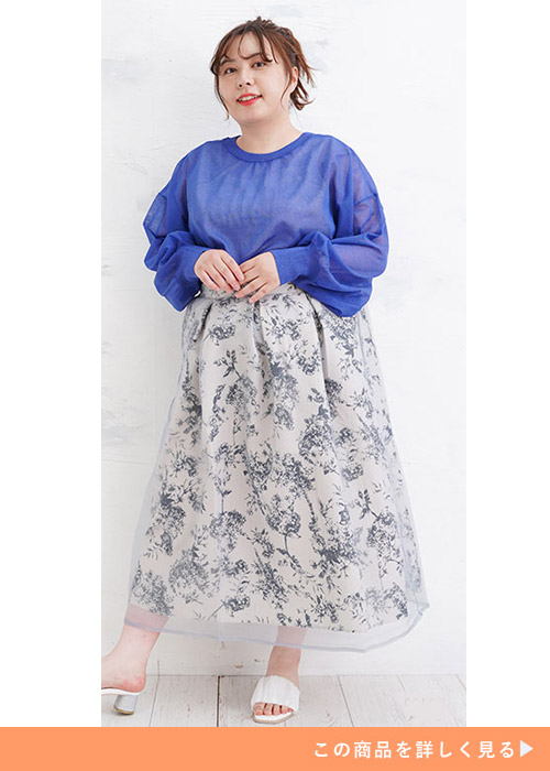 オーガンジーを重ねた花柄スカートに、ブルーのシアートップスの裾をインして着る女性