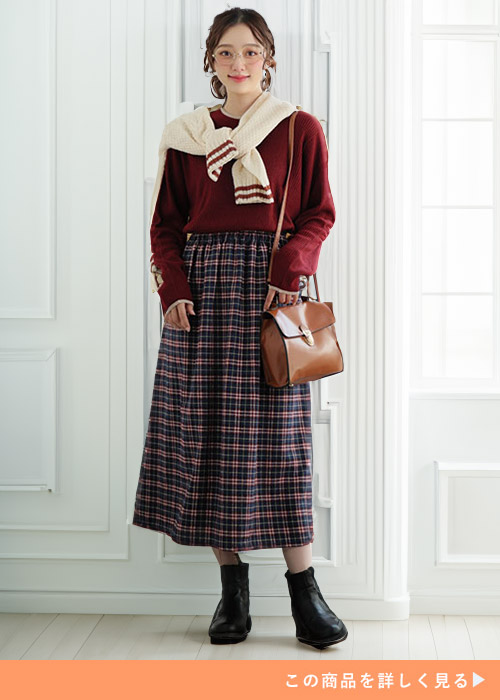 ボルドーのトップスに白のトップスを肩掛けし、チェック柄のフランネル素材スカートを履く女性