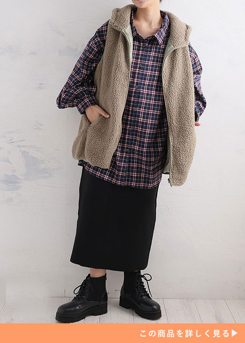 ネイビー×ボルドーのチェック柄シャツにベージュのもこもこベストを羽織り、黒のタイトスカートを履く女性