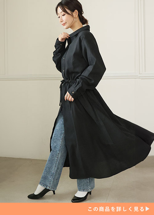 黒のロングシャツワンピースを着て、中にデニムパンツをはく女性