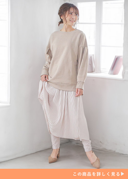 ピンクベージュのスカートにグレージュのレギンス、ベージュのトレーナーを着る女性